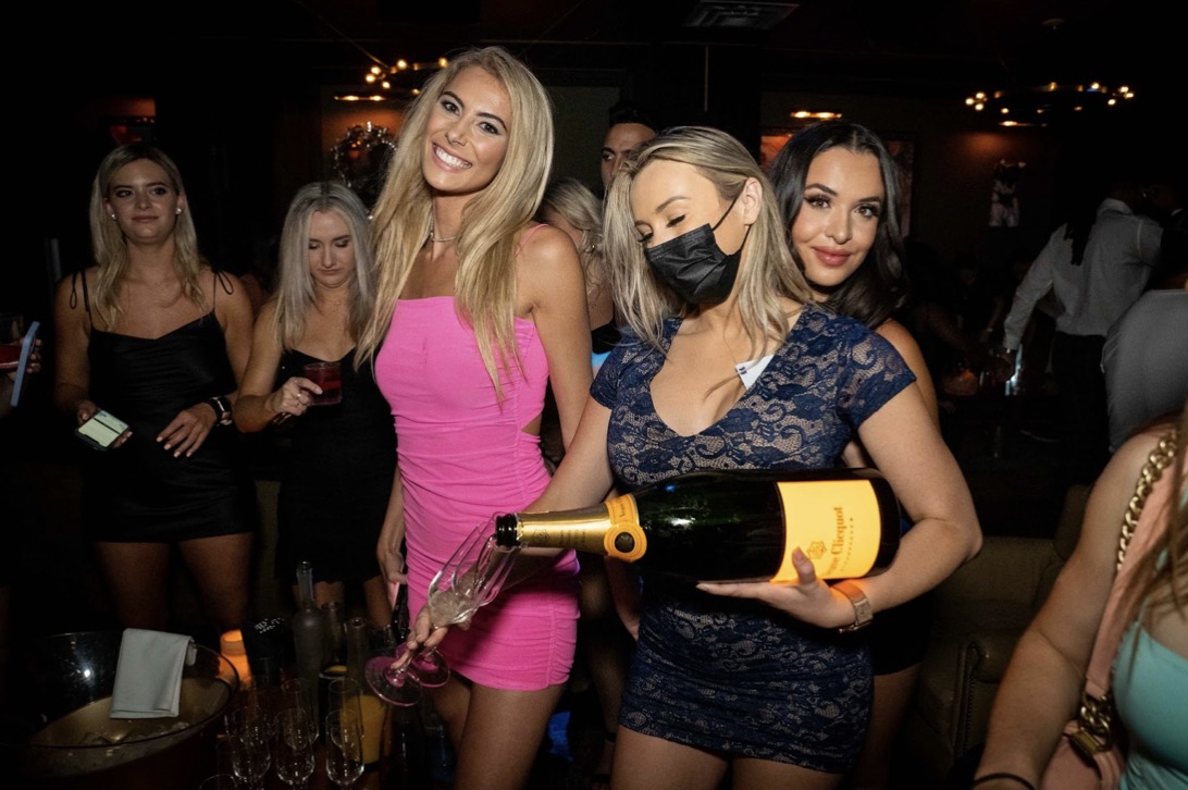 Women in a party, one holding a bottle of drink while pouring it in a glass