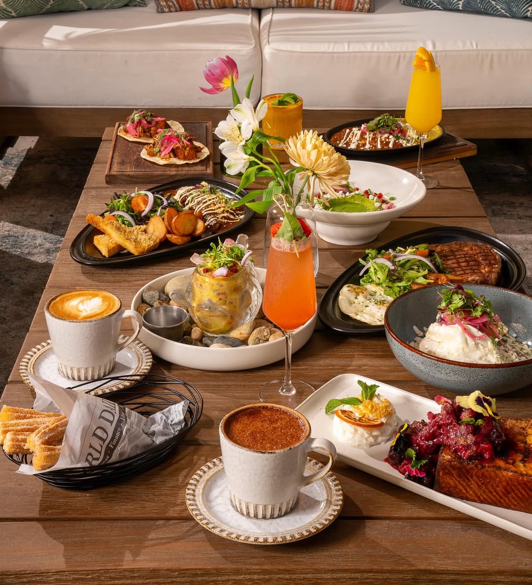A high-angle shot captures a wooden table laden with a variety of Latin American dishes and drinks