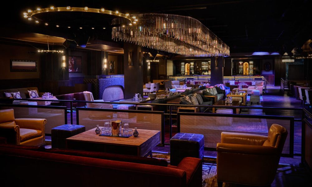 An intimate and sophisticated lounge with plush furnishings, a large, ornate chandelier, and a bar area in the background, likely the Oxford Social Club in San Diego.